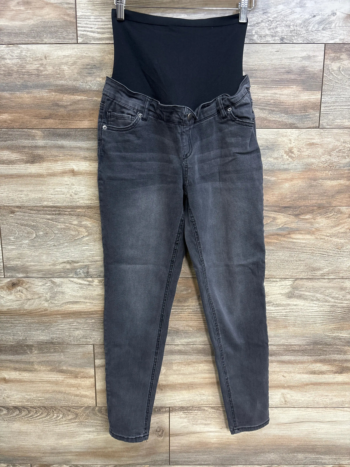 Front view of grey Time & Tru maternity jeans with black over-belly panel, pockets, and button fly on wood floor