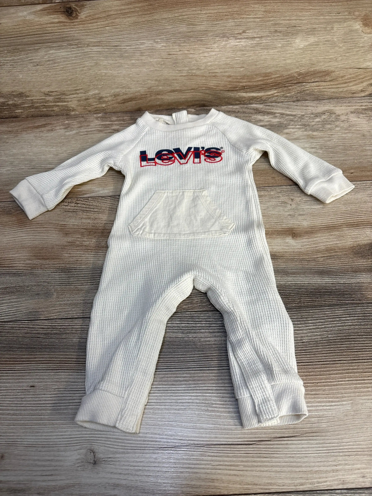 Cream long-sleeve Levi's baby romper with front pocket, laid flat on wood background