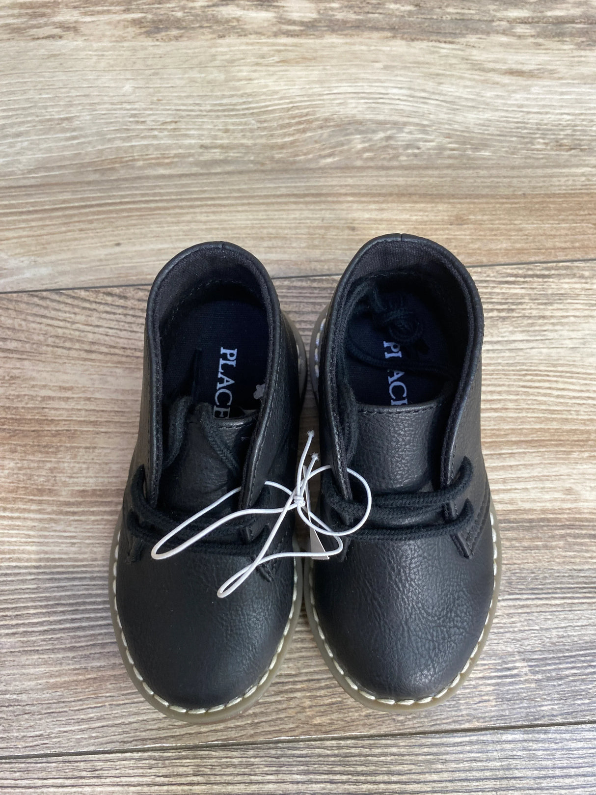 Black toddler lace-up shoes on wood floor, soft leather finish, white stitching detail