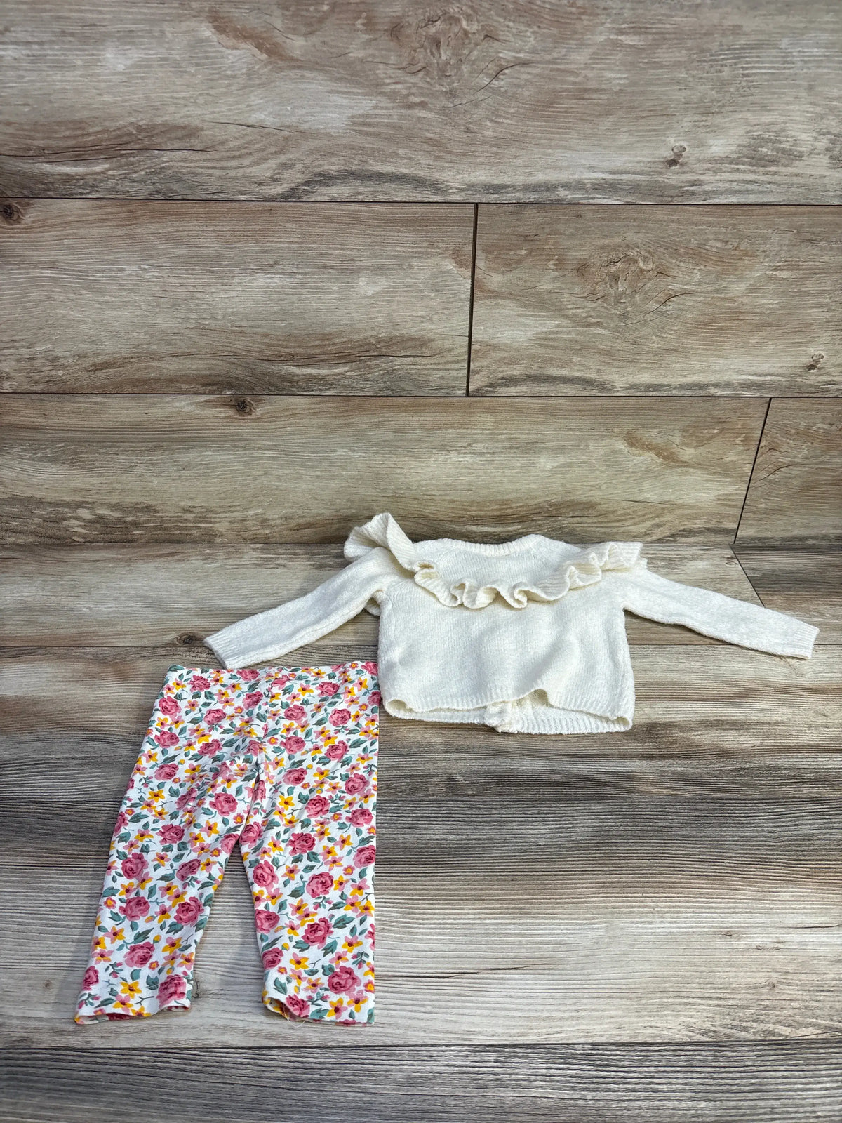 Flat lay of infant ivory knit ruffle cardigan and floral leggings showcasing ruffle collar and rose print on wood background