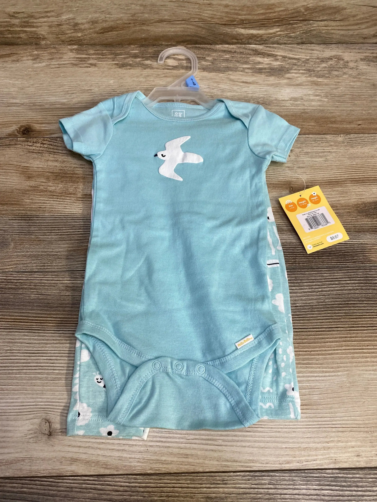 Flat lay of Hello Bello 2-piece blue bodysuit and pants with white bird applique, snap crotch, on wood background