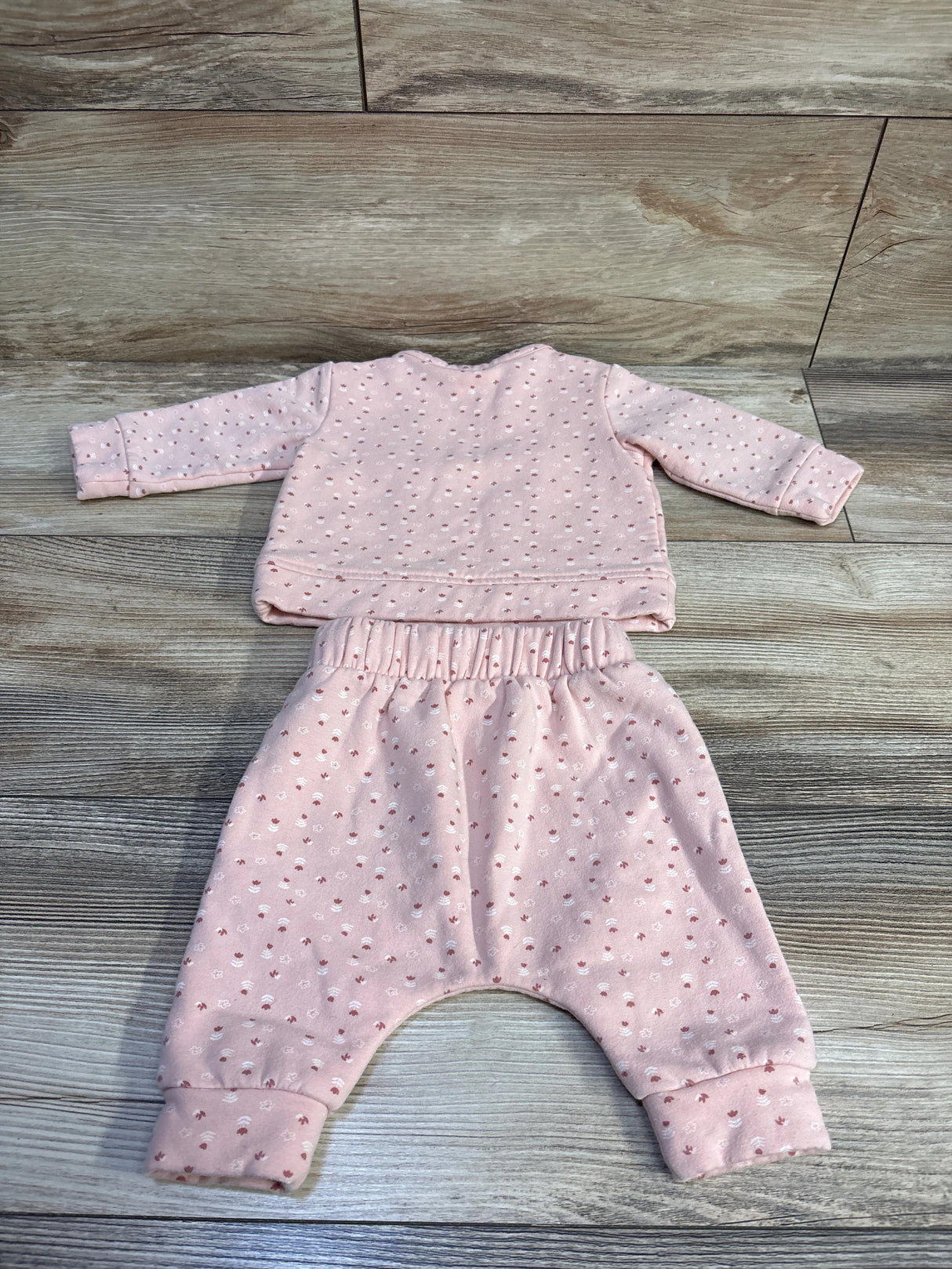 Flat lay of pink two-piece baby sweatshirt and pants set showing elastic waistband and cuffed ankles on wood background