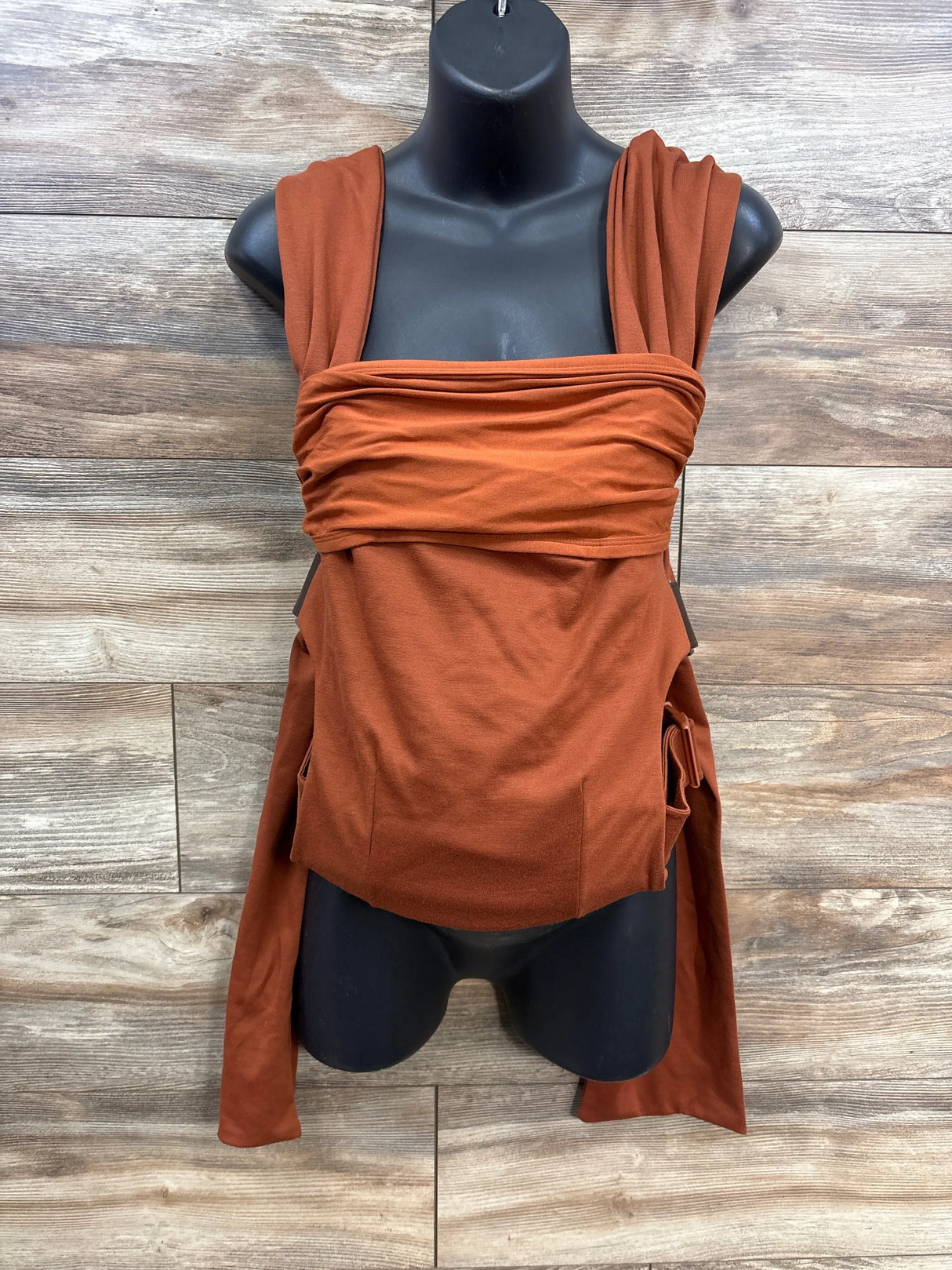 rust orange baby carrier wrap displayed on black mannequin torso against wood background