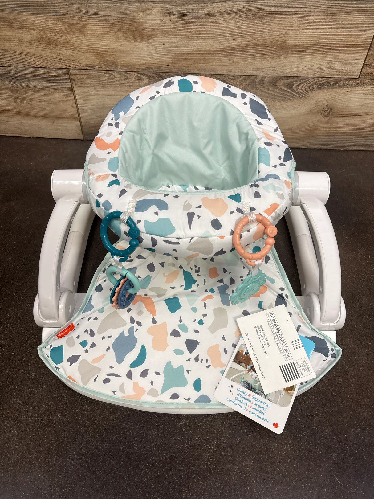 Fisher-Price baby seat with multicolor terrazzo pattern and attached toy rings on dark floor