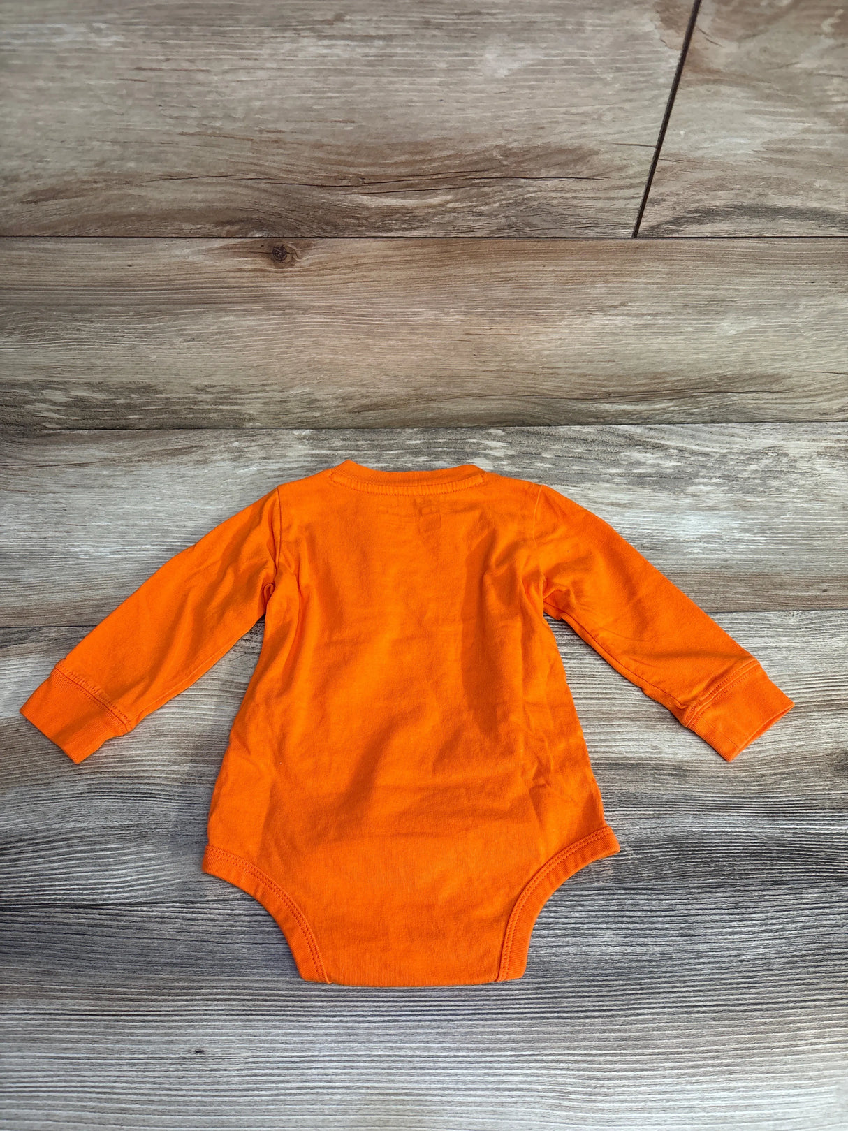 Bright orange long-sleeve baby bodysuit laid flat on wood-textured surface