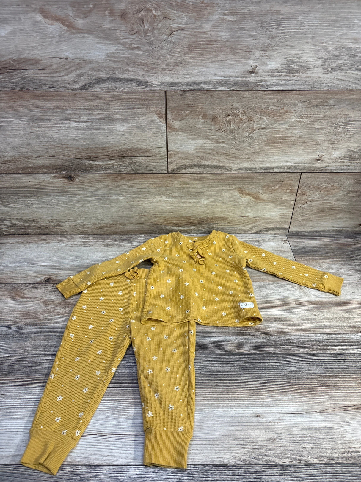 Flat-lay of yellow waffle-knit henley top and pants showing white floral print and cuffed ankles on wood background