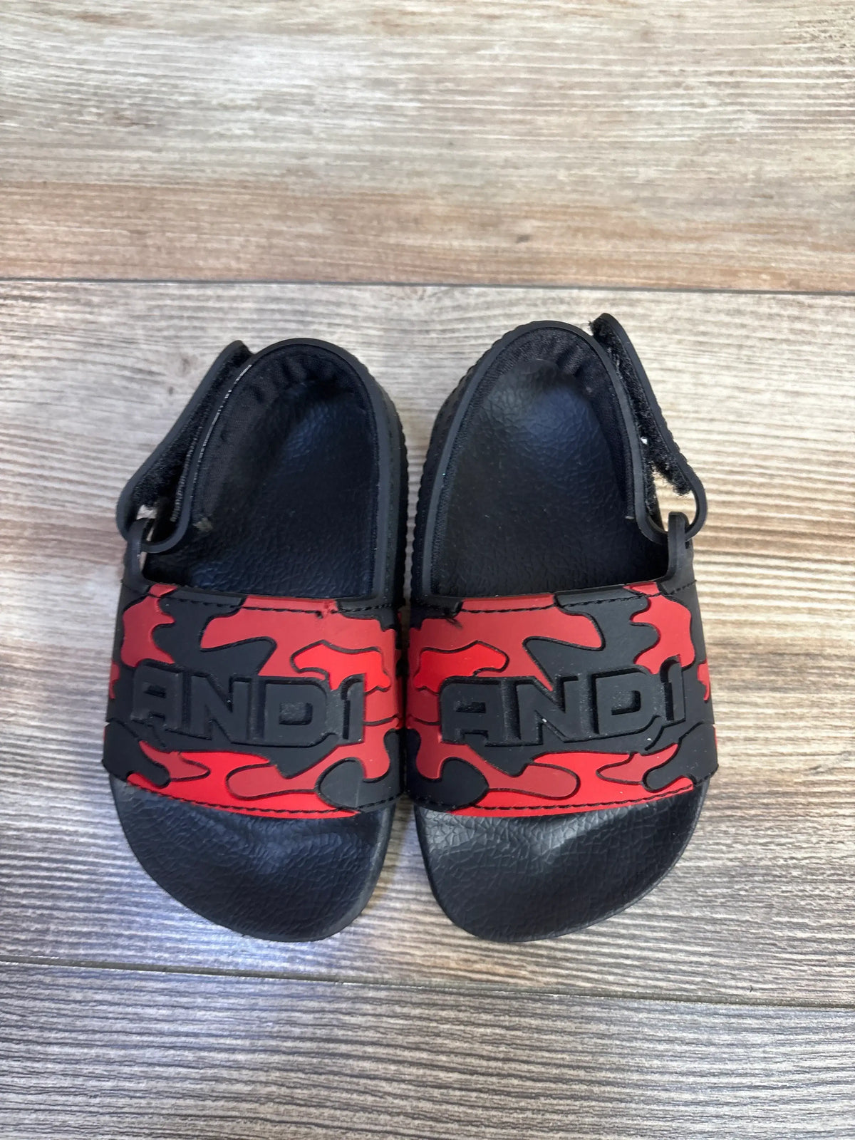 Top view of red camo AND1 slide sandals showcasing slip-on bands and black footbeds on a wood floor