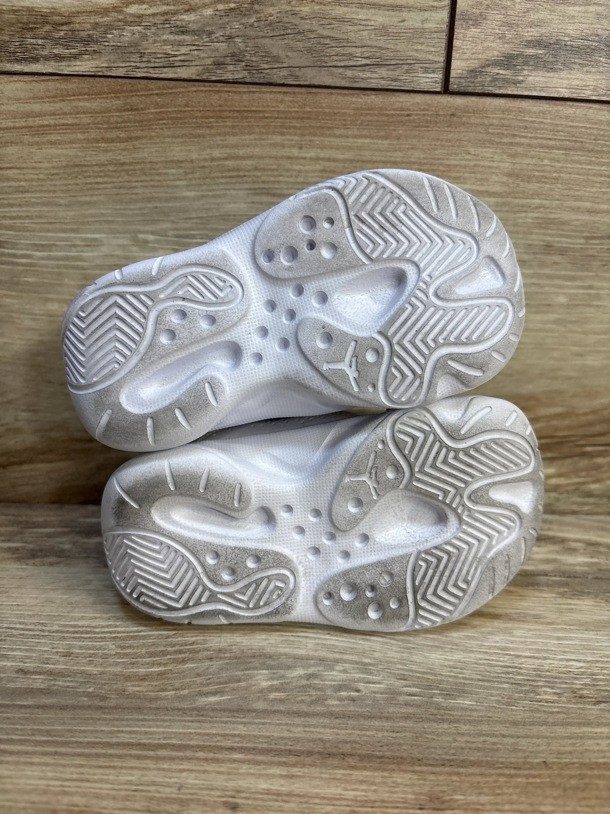 Pair of kids' white sneakers with textured rubber soles, gently used, on wood floor
