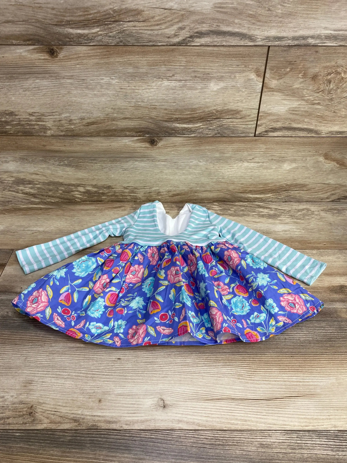 Flat lay of handmade blue baby dress with mint-white striped bodice and bright floral skirt, size 12-18m on wood background
