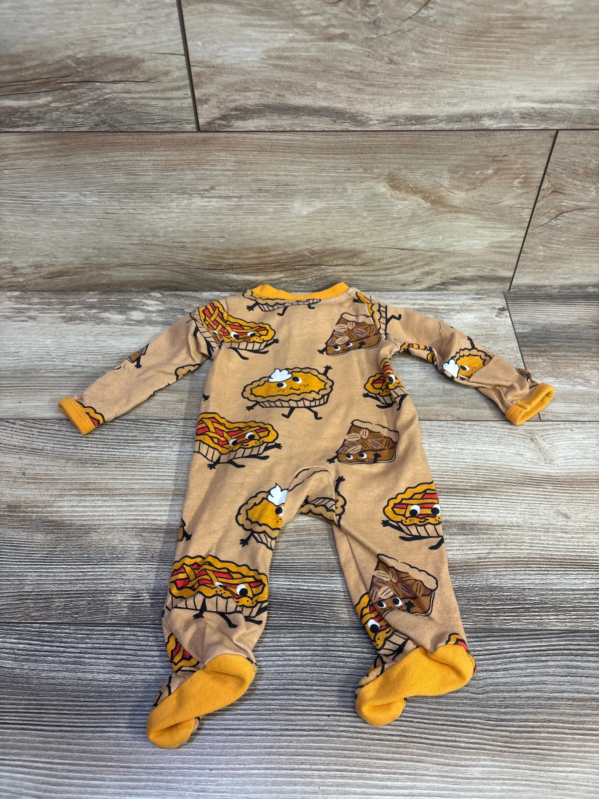 Back view of newborn footed sleeper with orange trim and pie print on tan fabric laid flat on wood floor