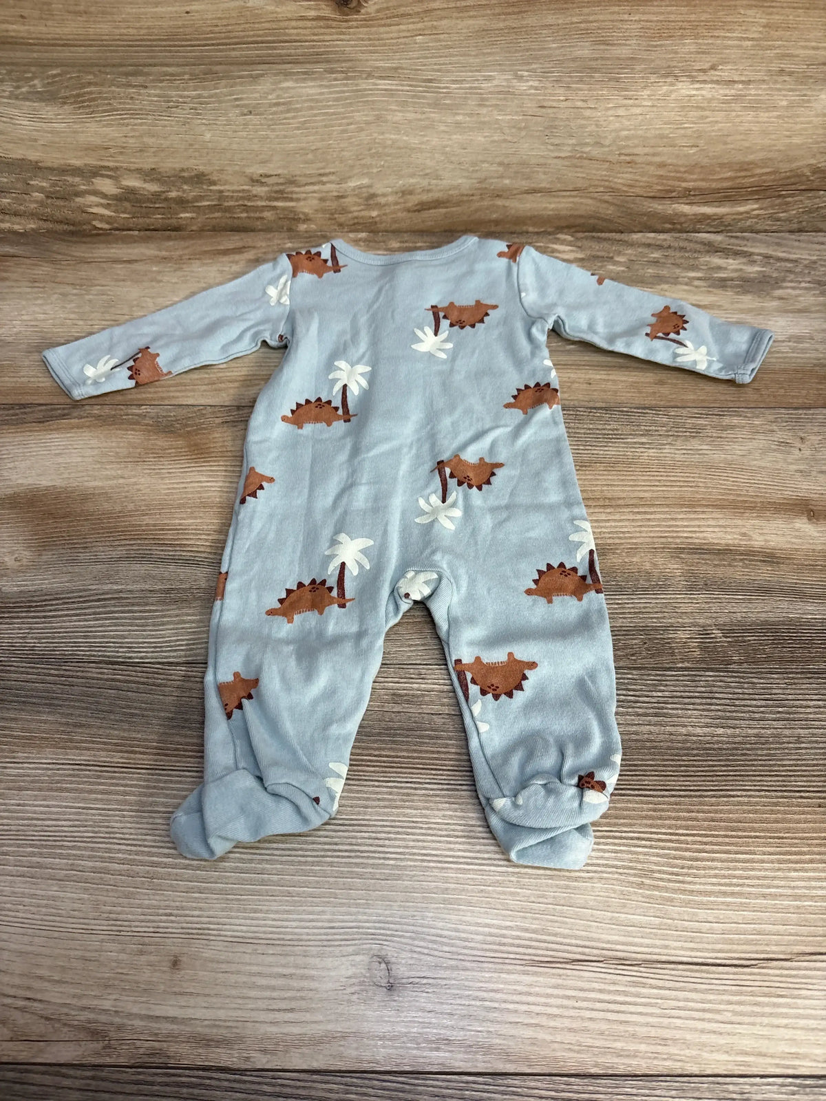 Flat lay of Carter’s dinosaur sleeper size 3m showcasing light blue footed pajamas with brown stegosaurus and palm tree print on wood plank floor