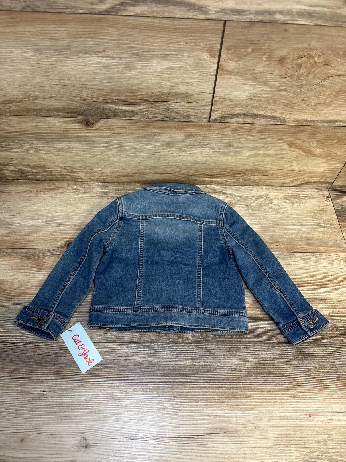 Kids' blue denim jacket, long sleeves, displayed flat on wood floor, Cat & Jack tag visible