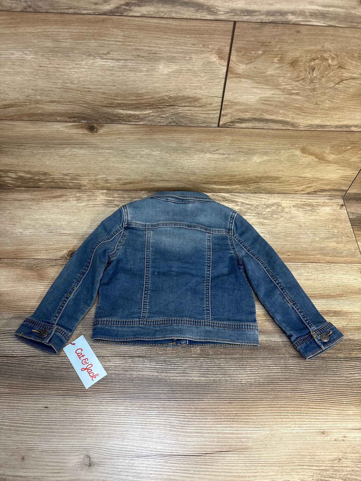 Kids' blue denim jacket, long sleeves, displayed flat on wood floor, Cat & Jack tag visible