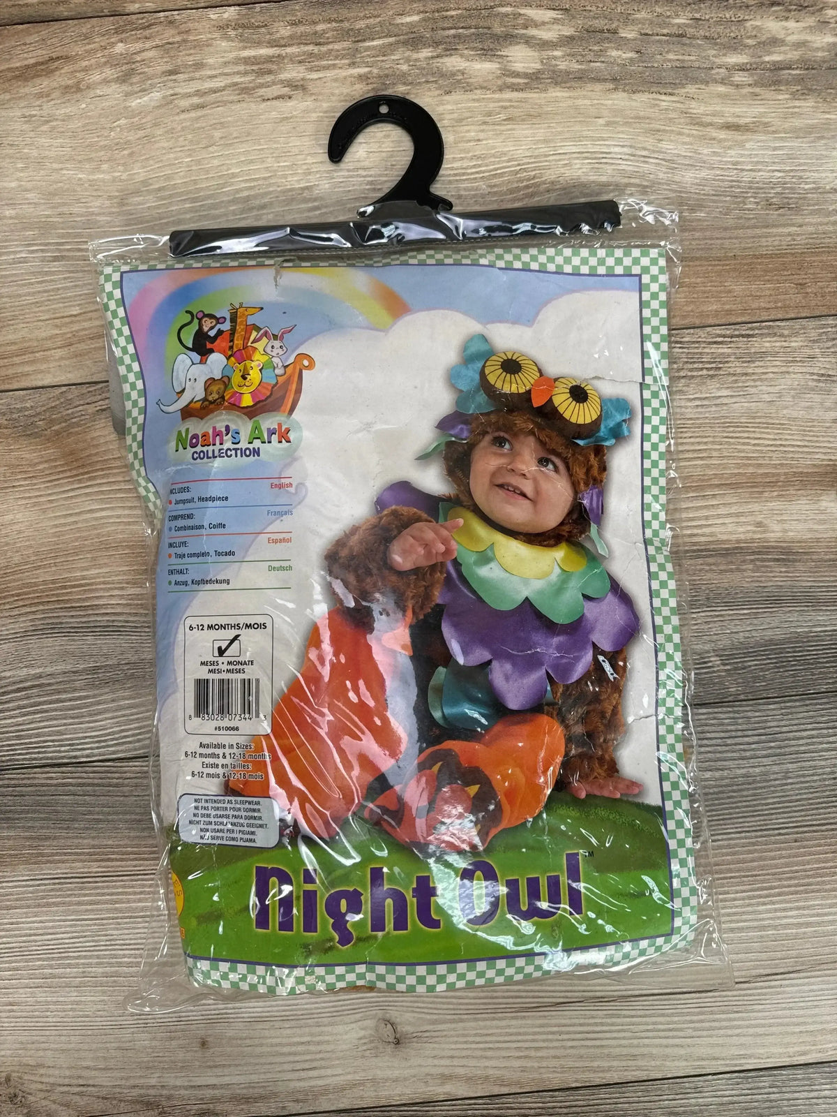 Front view of packaged Night Owl baby costume showcasing owl headpiece and purple layered feather bodysuit on wooden floor