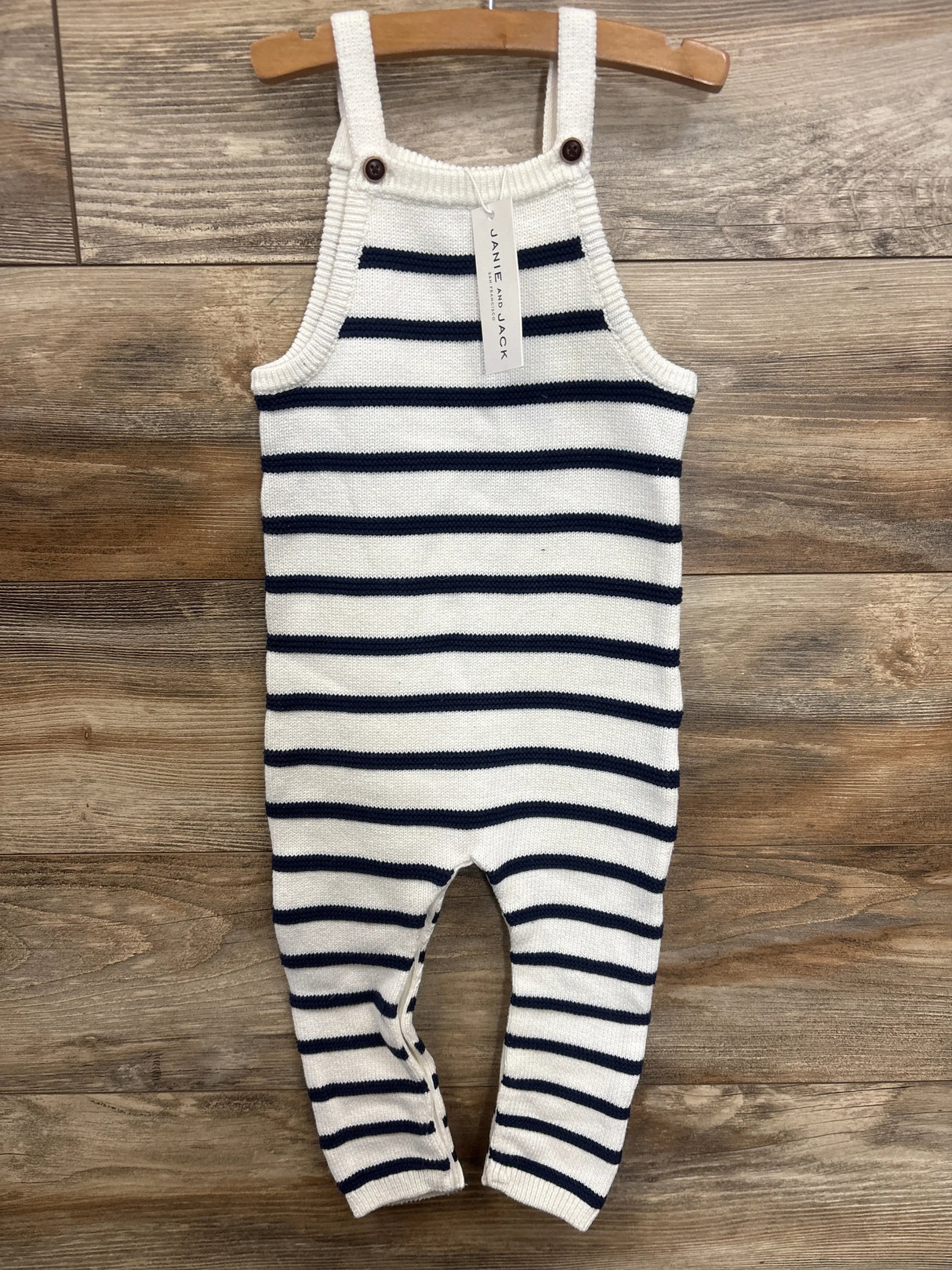 Front view of Janie & Jack striped knit overalls in white and navy, showing wooden button shoulder straps on wood plank background