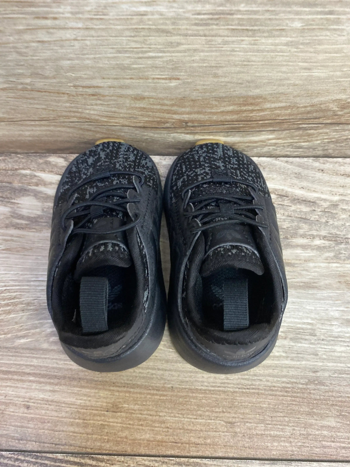 Pair of black toddler sneakers with laces on wood background, gently used kids shoes