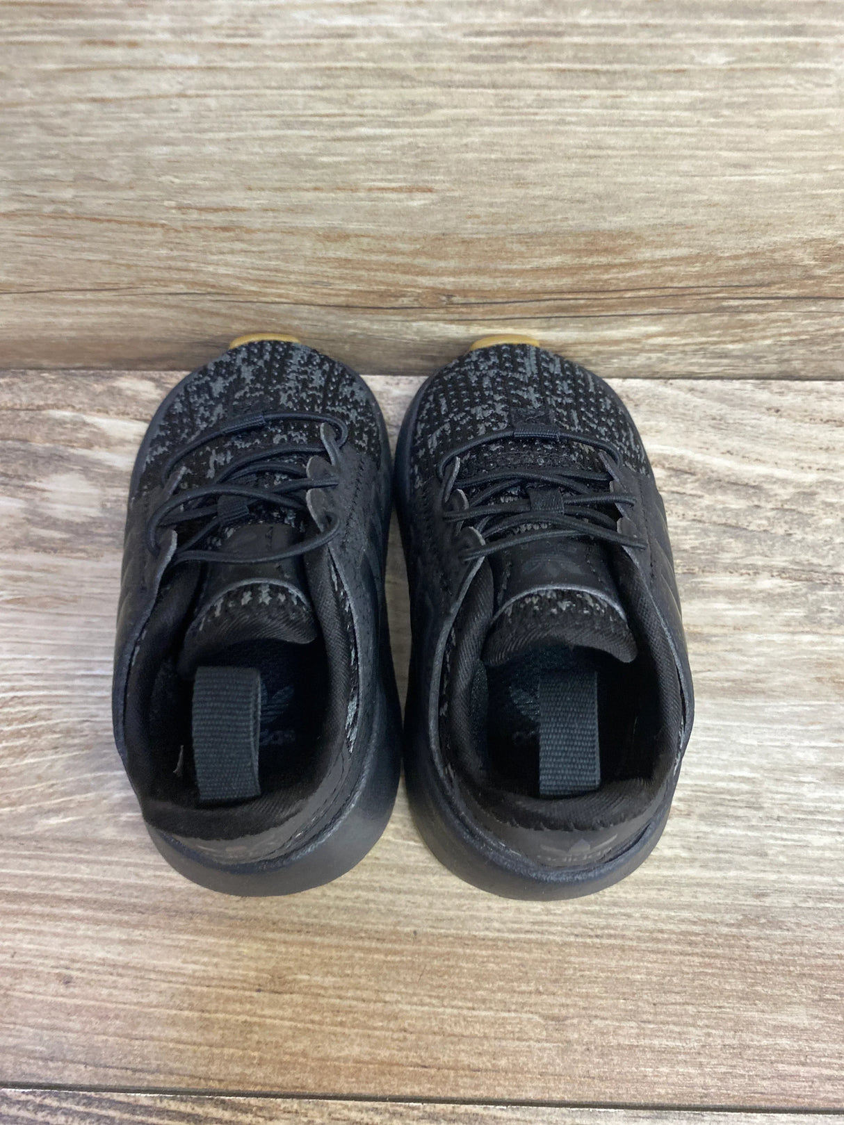 Pair of black toddler sneakers with laces on wood background, gently used kids shoes