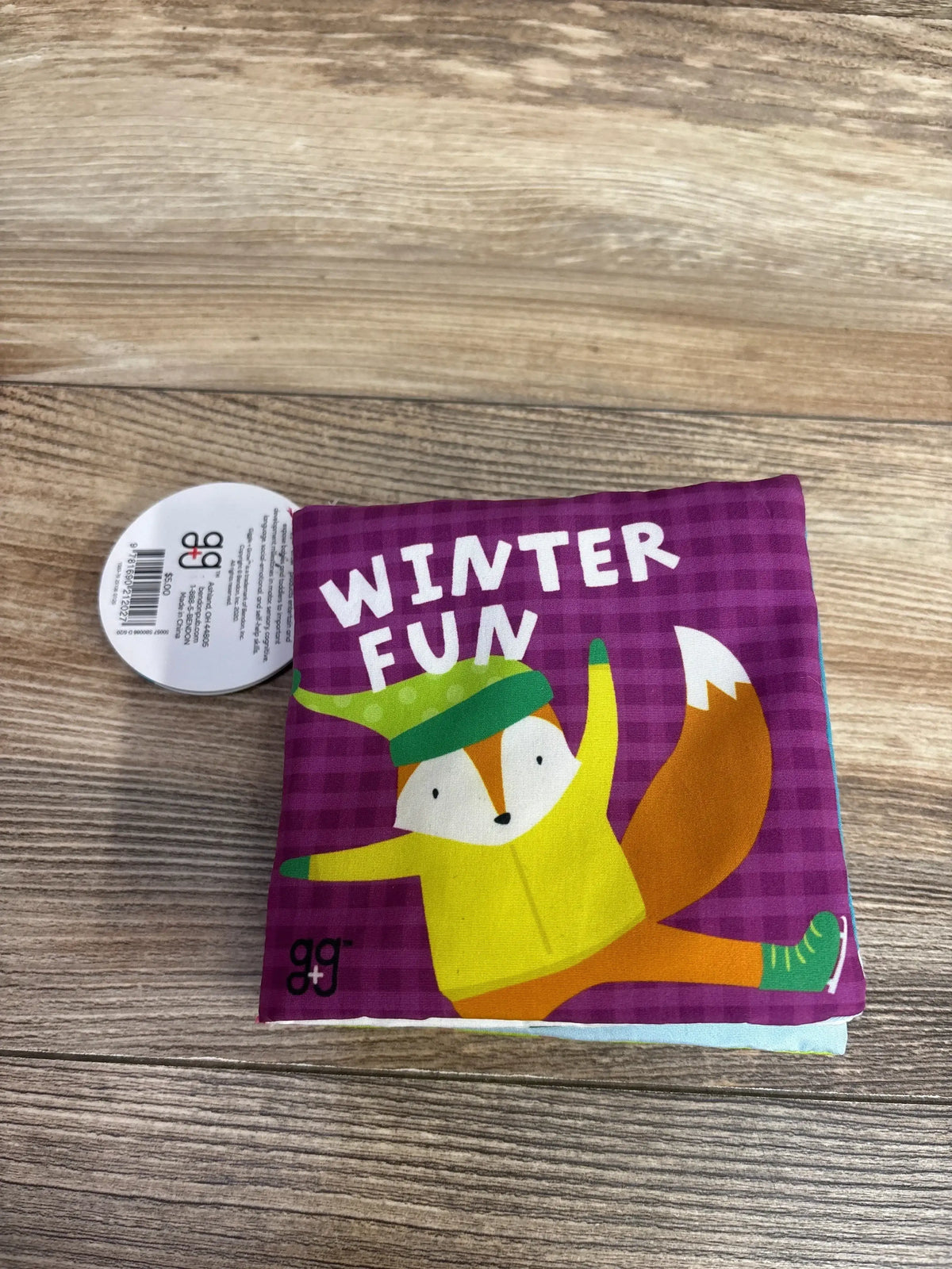 Children's soft fabric book titled Winter Fun with cartoon fox wearing winter clothes on wooden surface