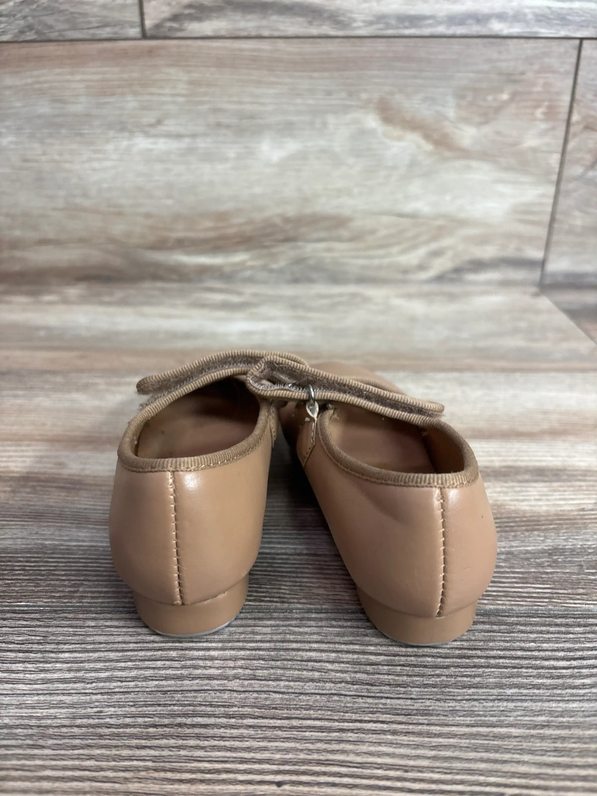 Rear view of tan children's tap shoes (size 9C) showcasing elastic strap and low heel with wood plank background