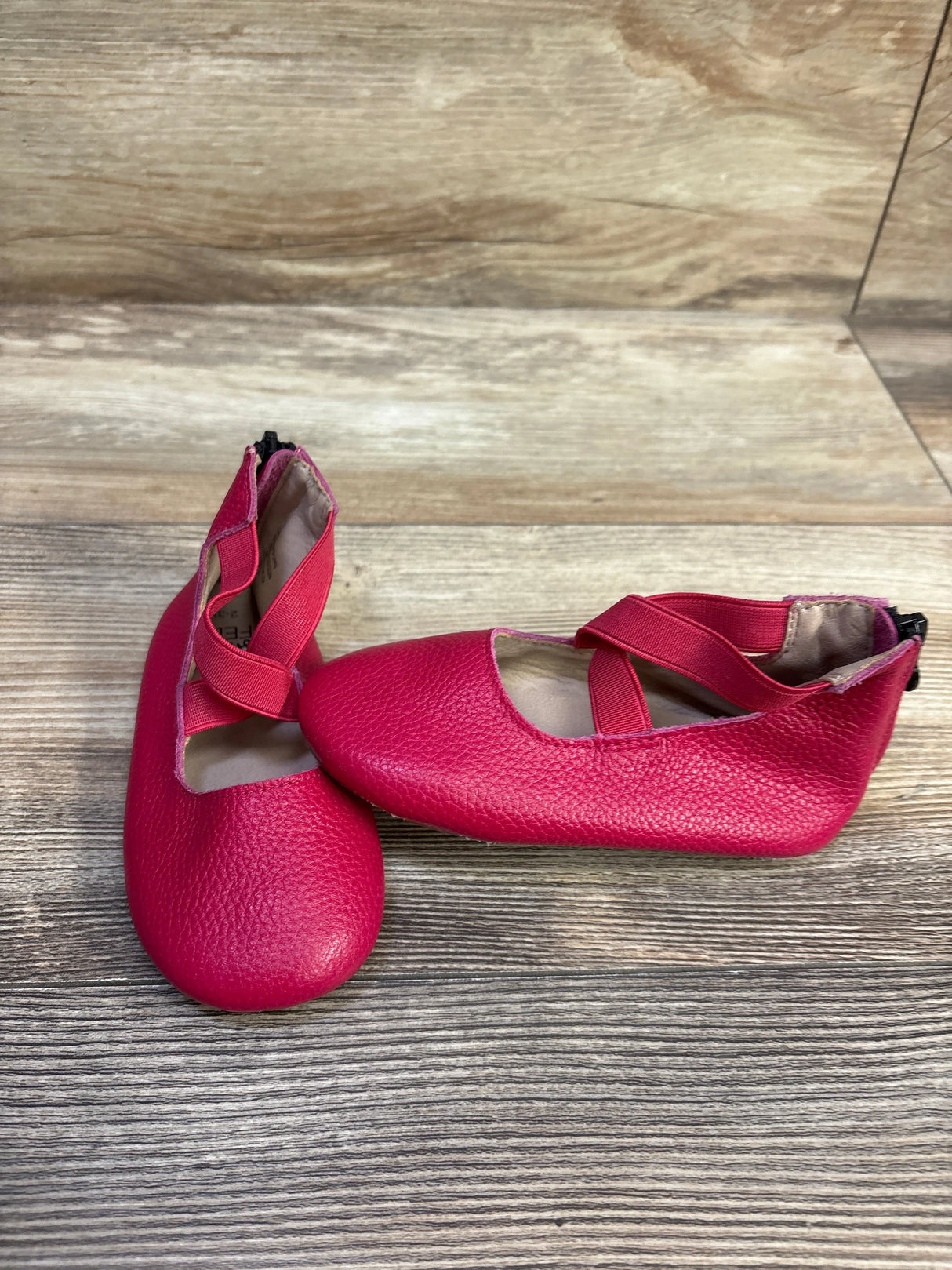Angled top view of pink Monkey Feet Mary Jane flats with criss-cross straps and pebbled texture on wood