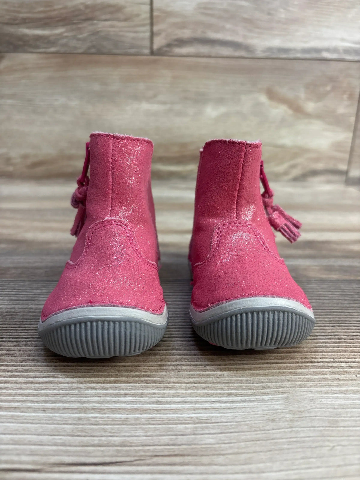 Front view of Stride Rite Zoe toddler ankle boots showing pink suede with tassel accents and gray soles on wood background