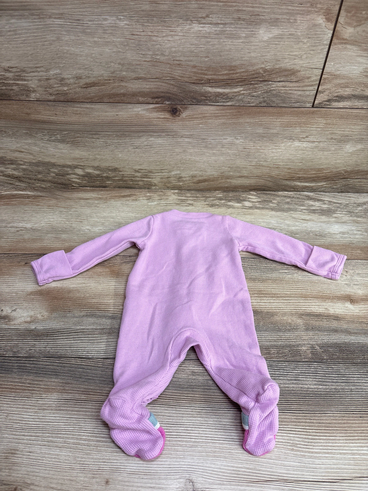 Front view of a pink Just One You waffle-knit footed sleeper in newborn size with long sleeves on a wood-look floor