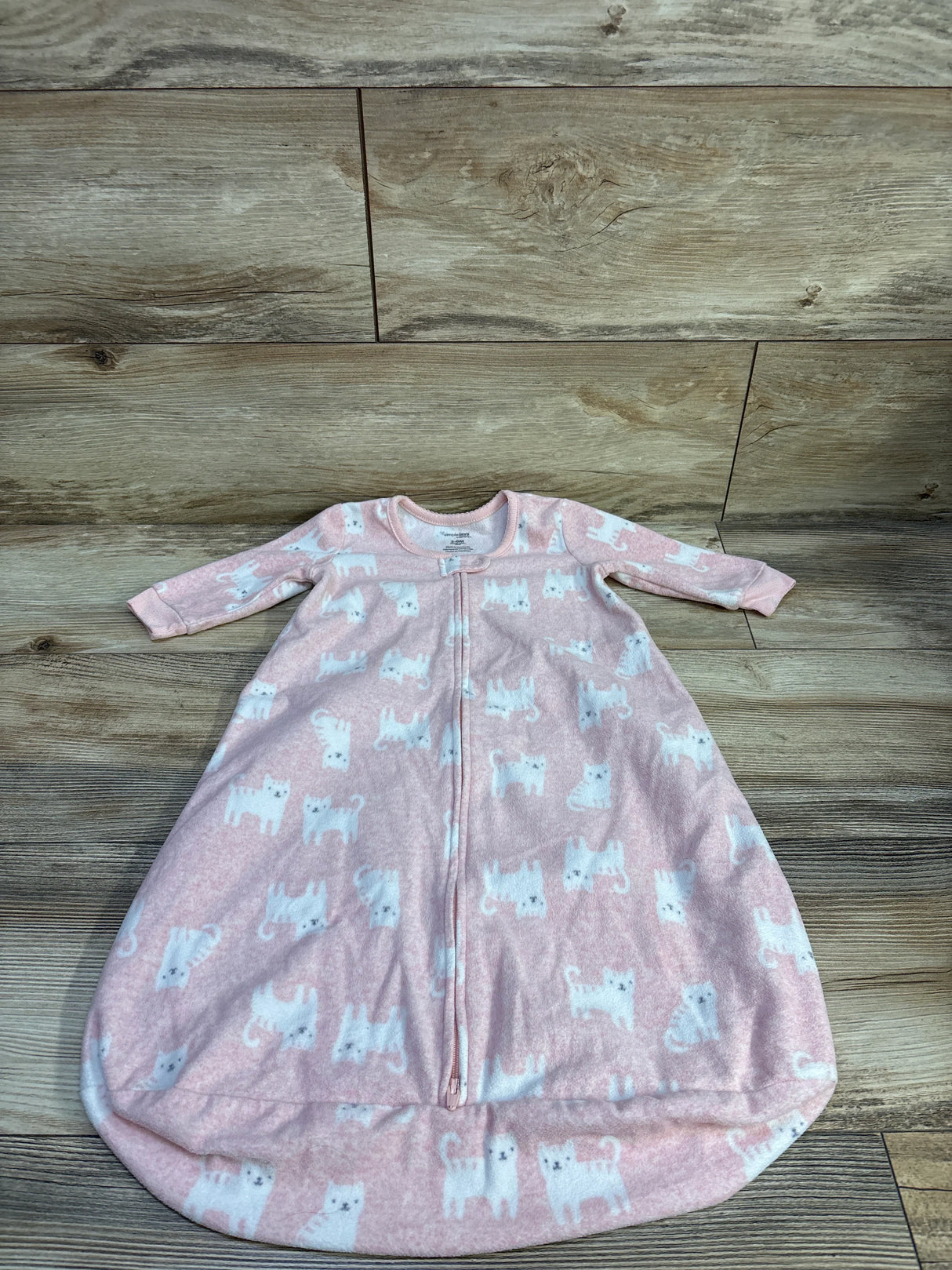 Flat lay of Simple Joys pink baby sleep sack showing white cat print, front zipper and long sleeves on wood background