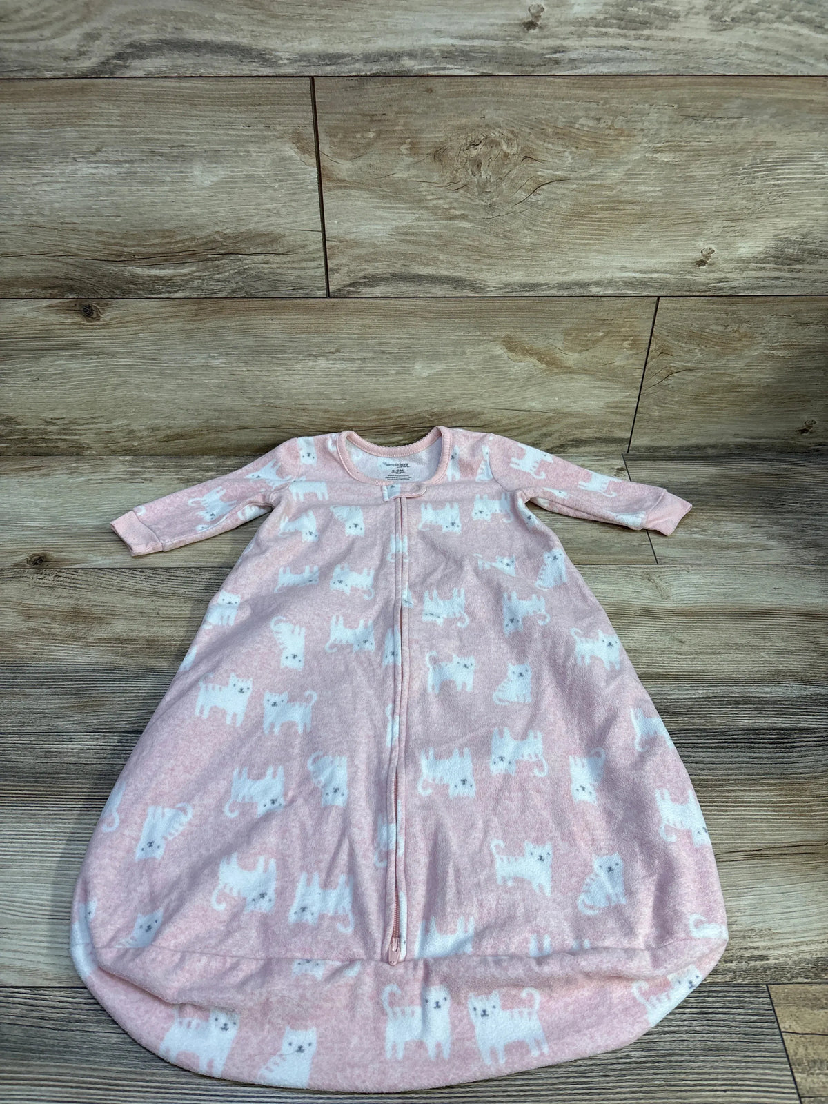 Flat lay of Simple Joys pink baby sleep sack showing white cat print, front zipper and long sleeves on wood background