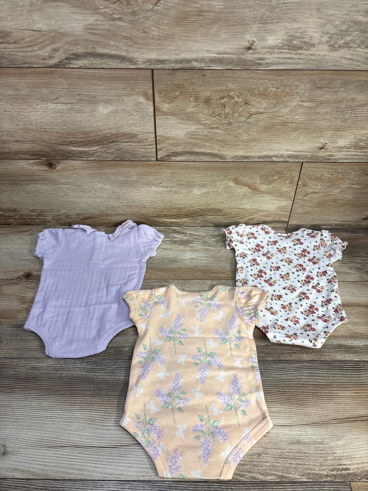 Three Nicole Miller puff sleeve baby bodysuits in purple, peach floral, and white floral prints.