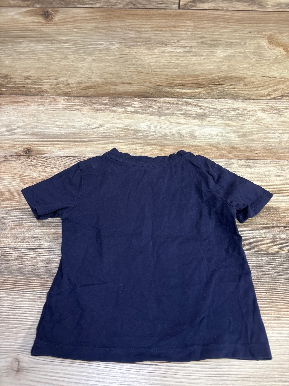 Back view of navy Baby Gap logo shirt in size 18 months showcasing short sleeves on a wood-look background