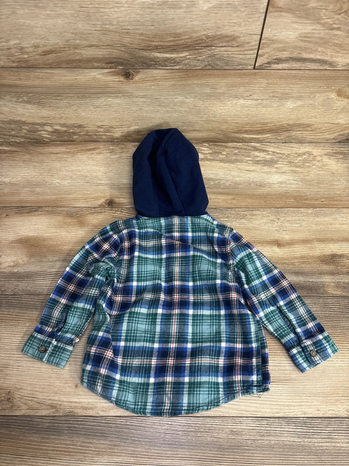 Kids green plaid flannel shirt with navy hood, long sleeves, laid flat on wood floor