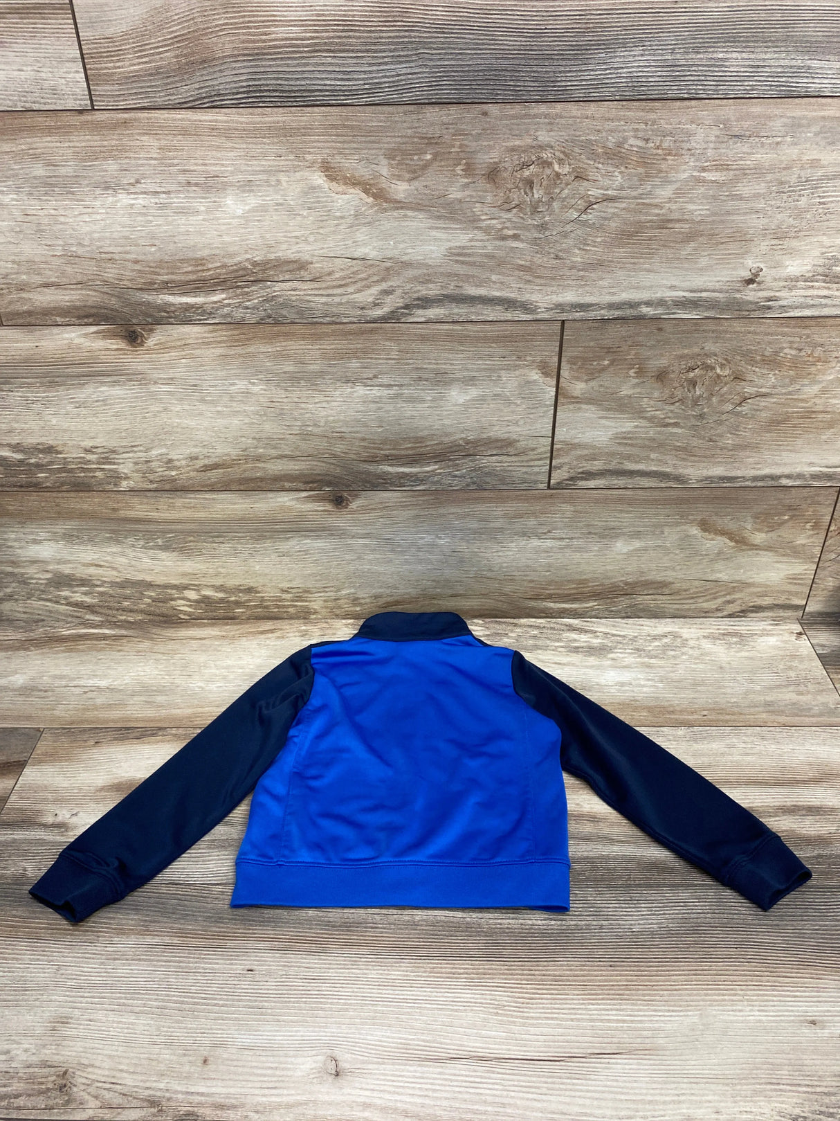 Back view of a blue and navy long-sleeve kids jacket laid flat on wooden floor