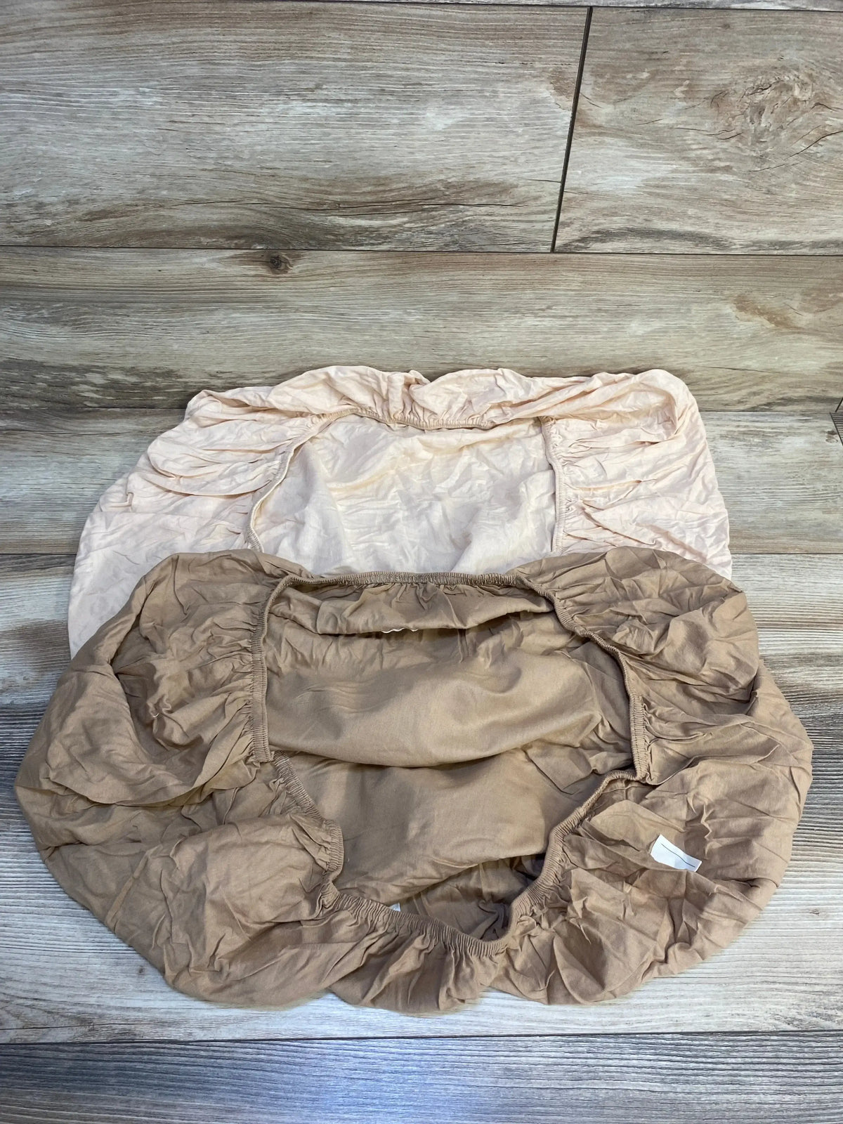Overhead of KeaBabies Soothe changing pad covers 2-pack, neutral tan and pale pink fitted covers with elastic edges on wood floor