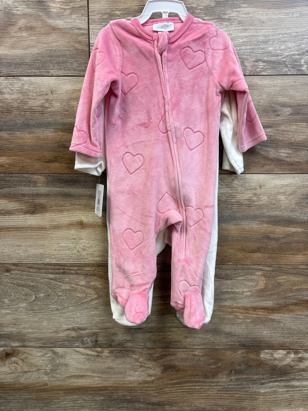 Front view of Sterling Baby blanket sleepers with pink heart patterns and covered feet on a wood-grain background