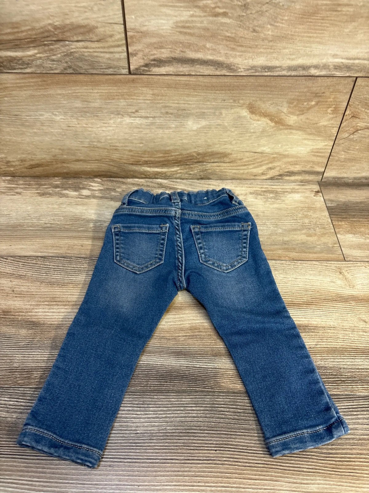 Back view of Children’s Place blue toddler legging jeans showcasing two rear pockets and adjustable waistband on wood flooring