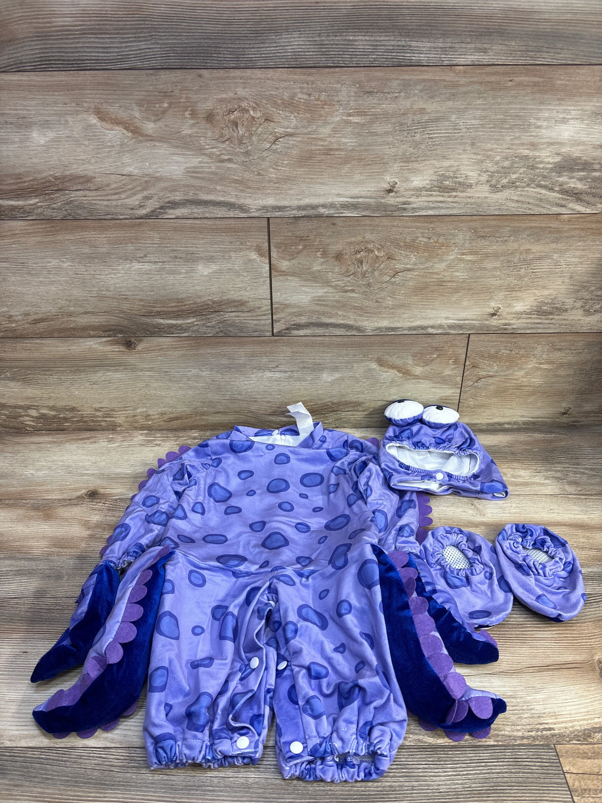 Front of purple 3-piece baby octopus costume (12M) with tentacle sleeves, plush hat and booties on wood background