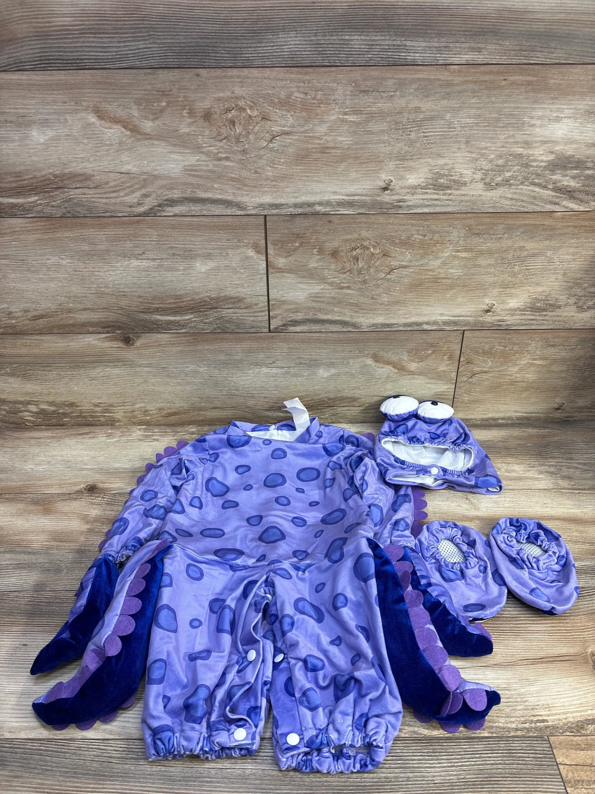 Front of purple 3-piece baby octopus costume (12M) with tentacle sleeves, plush hat and booties on wood background