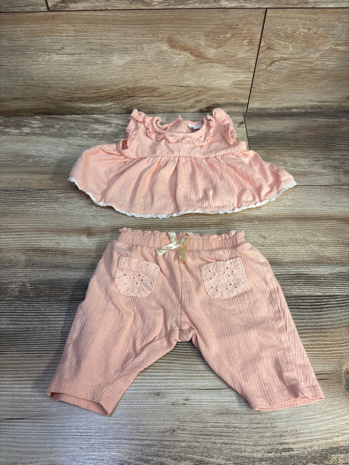 Flat lay of peach Nicole Miller 2pc gauze set showing ruffled peplum top, lace hem and elastic-waist pants on wood background