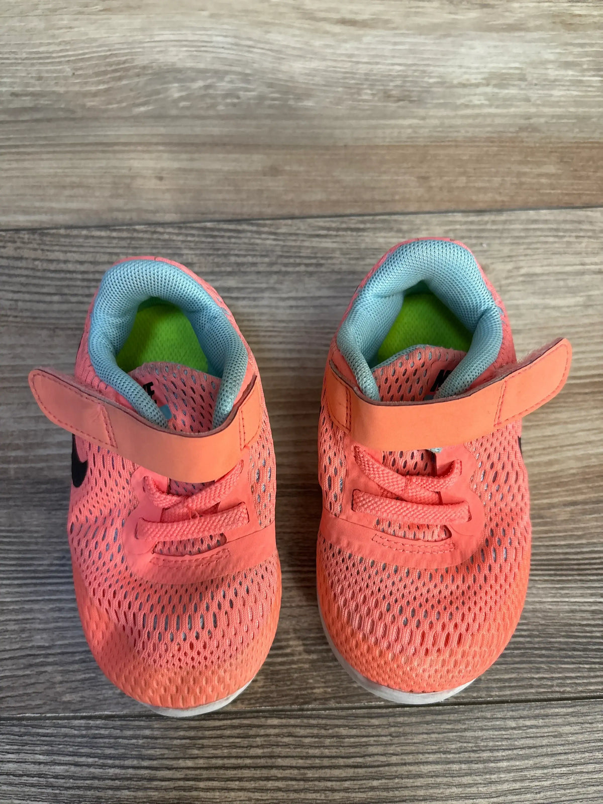 Top view of Nike Free Run sneakers showcasing coral mesh upper with black swoosh and Velcro strap on wood plank floor