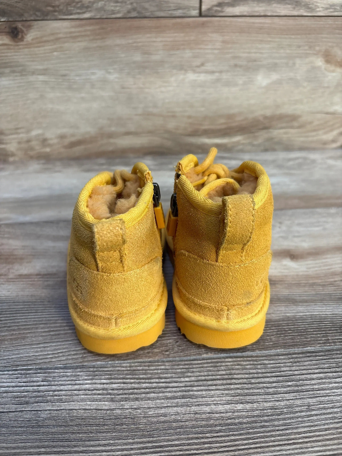 Back view of yellow suede toddler boots with fluffy interior on wooden surface