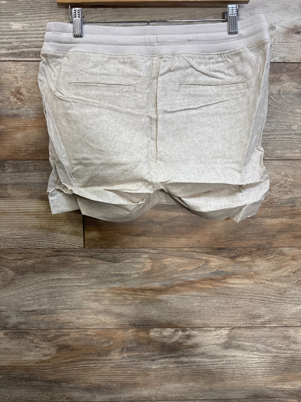 Back view of beige maternity linen-blend shorts showcasing elasticized under-belly waistband and back welt pockets on wood