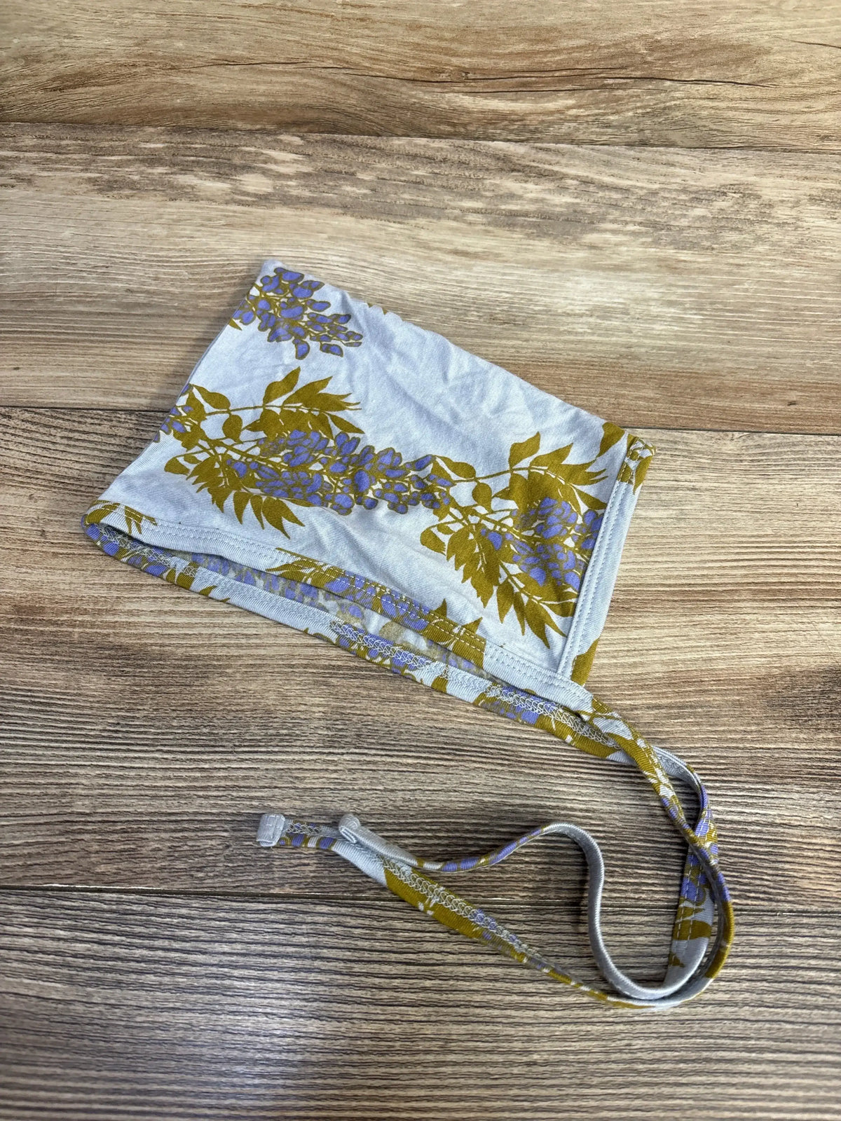 Top view of Kate Quinn blue bonnet in size 12-18m showcasing floral print and tie straps on a wood-grain background
