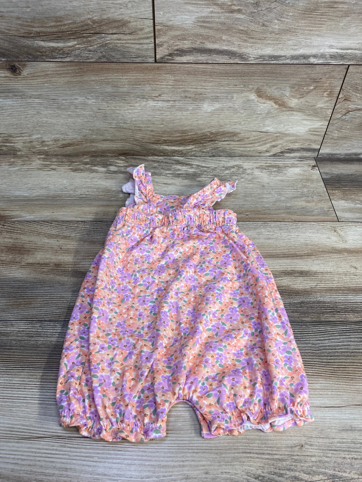 Floral baby romper with ruffled straps on wood floor background