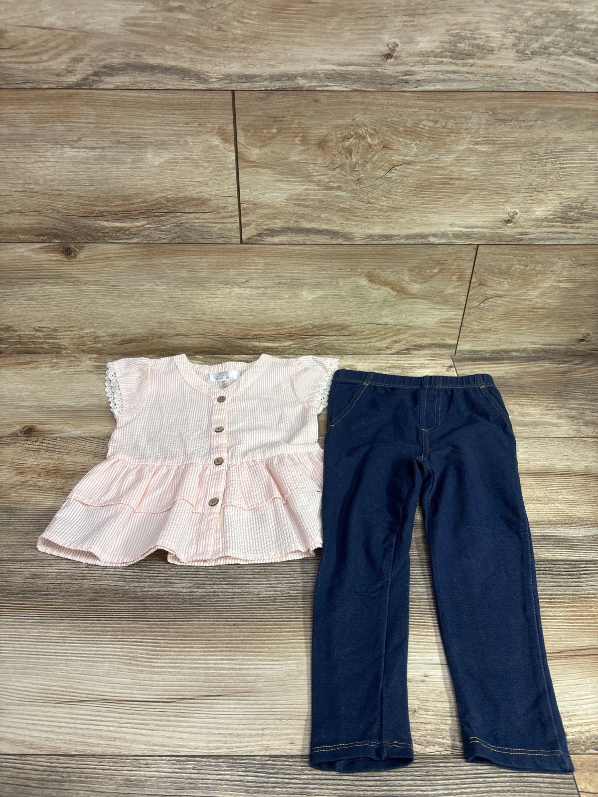 Front view of Koala Kids pink 2pc seersucker peplum top and jeggings set with lace-trimmed sleeves on wood