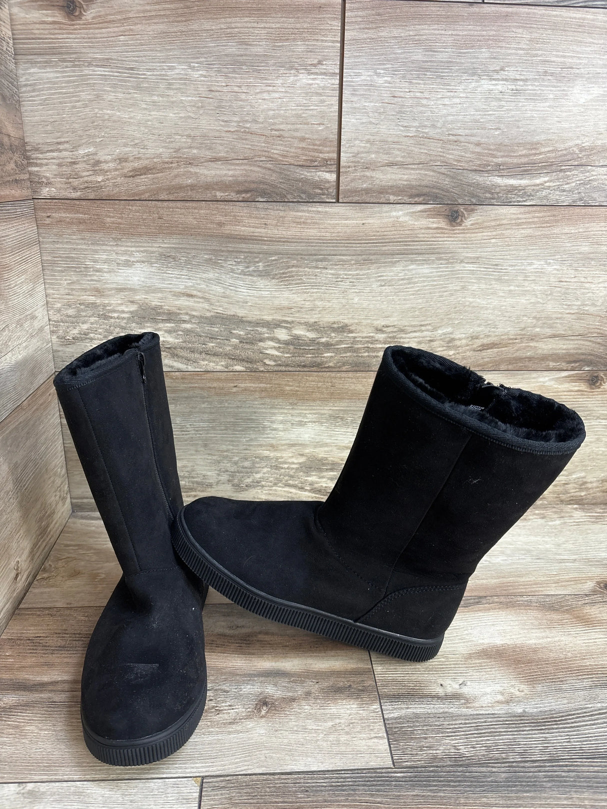 Black suede kids winter boots with faux fur lining on wood floor background