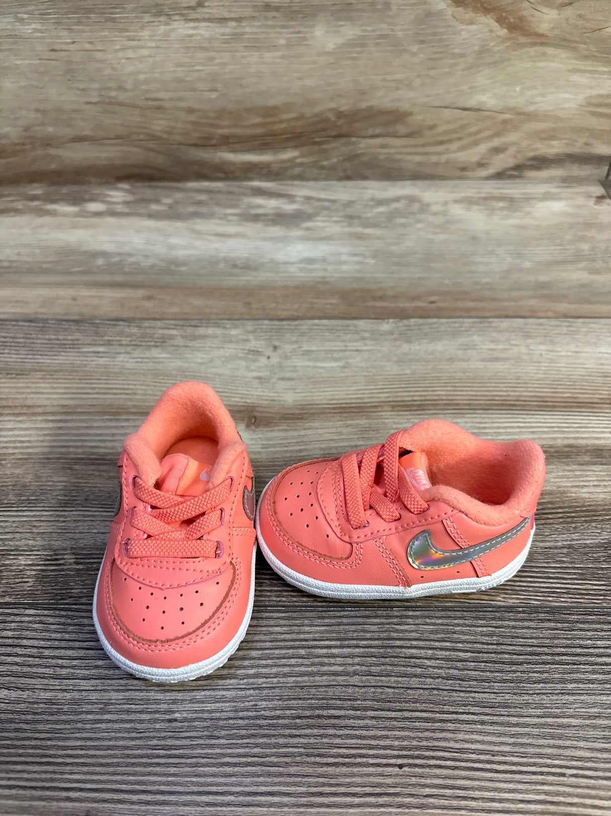 Front and side view of Nike Force 1 CB toddler sneakers showcasing iridescent metallic Swoosh with wood plank background
