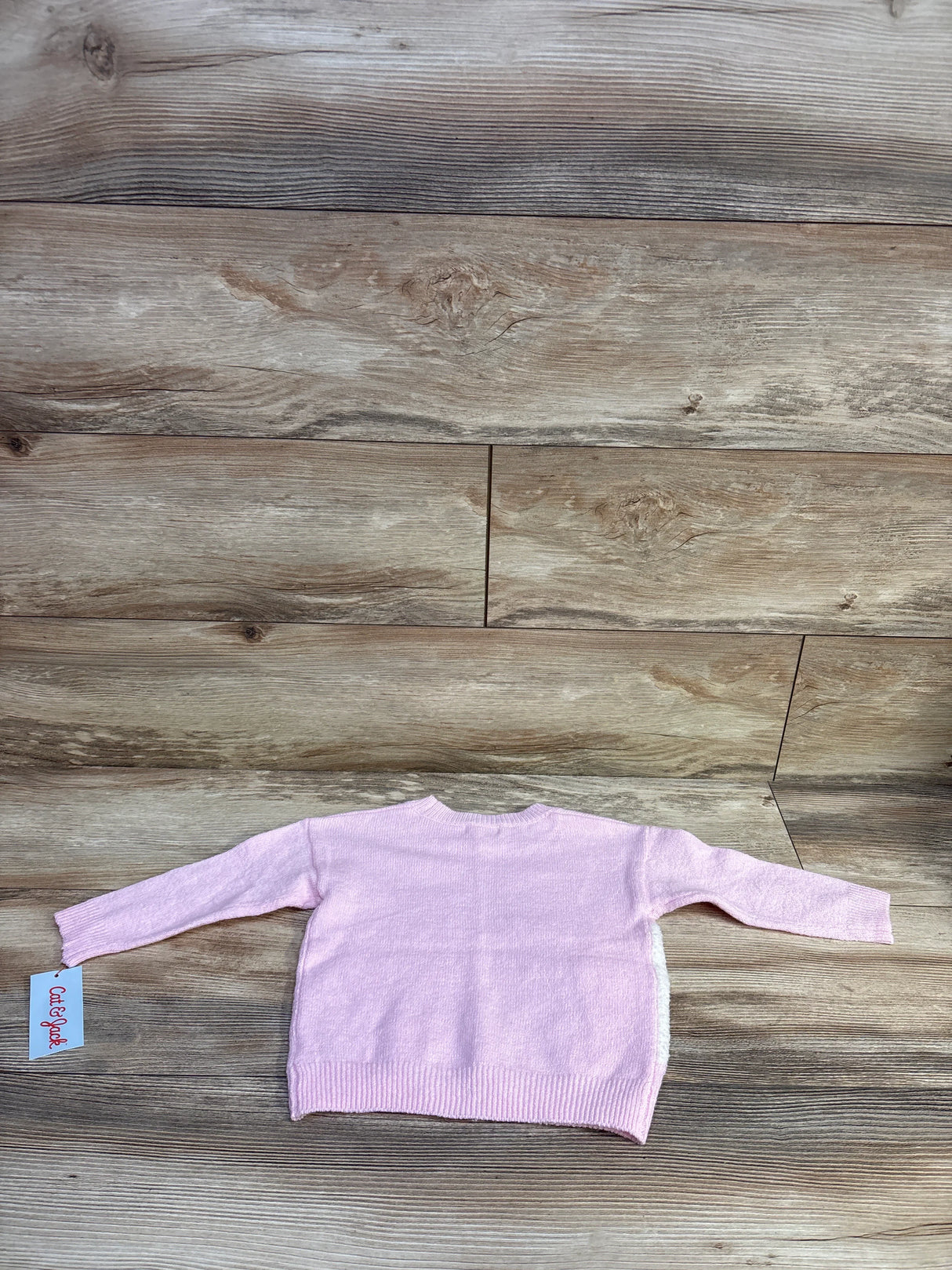 Back view of Cat & Jack pink knit toddler sweater showing ribbed hem, long sleeves, and brand tag on wood background