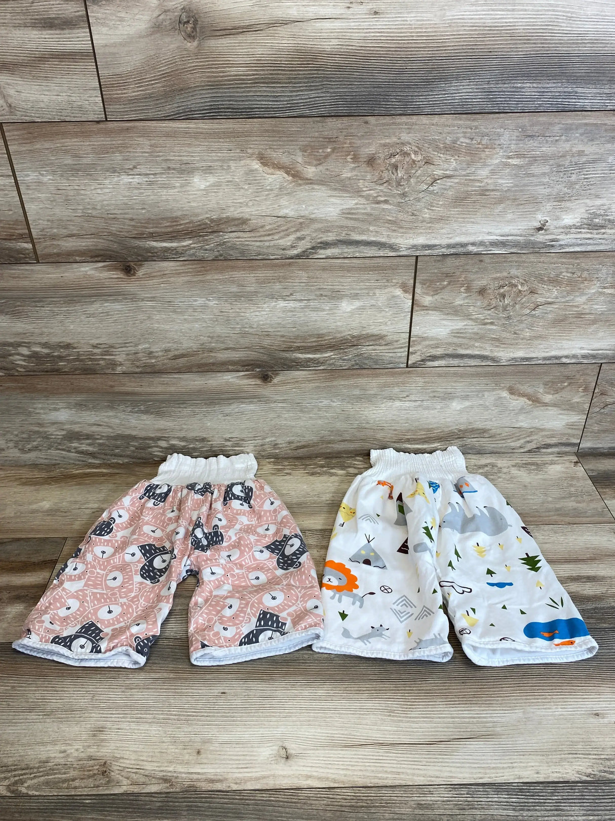 Top-down view of MooMoo Baby 2-pack training pants, pink patterned and white patterned, showing elastic waist on wood background