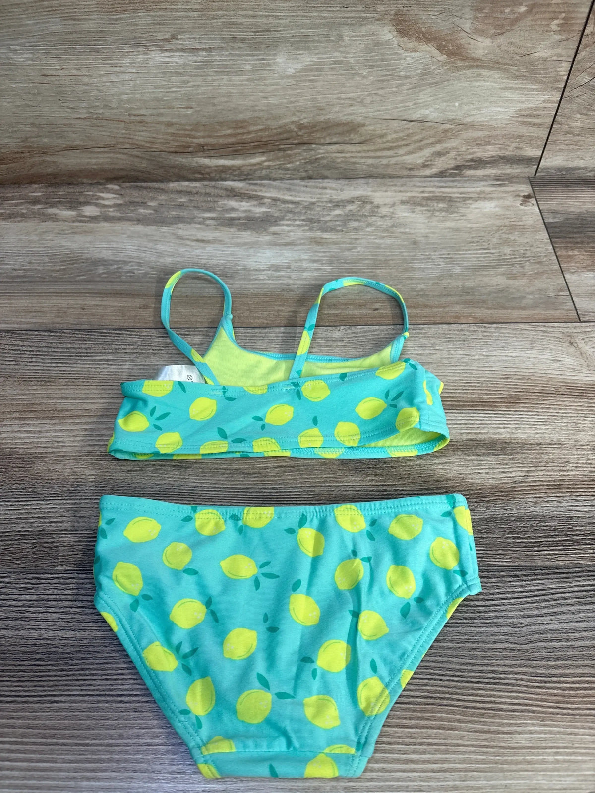 Flat lay of toddler teal two-piece bikini with yellow lemon print, crop top with thin straps and matching brief on wood