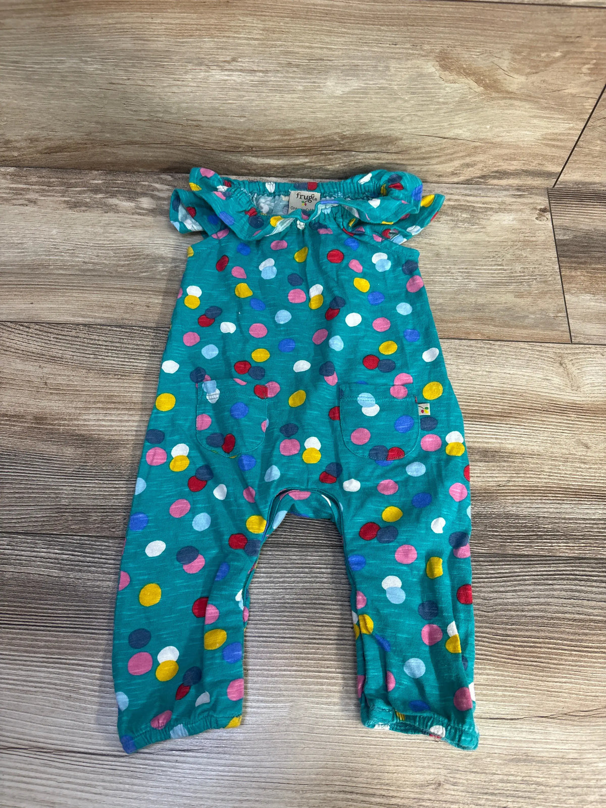 Front view of Frugi Organic Polka Dot Playsuit, size 0-3 months, showcasing ruffled sleeves and two pockets on a wood floor